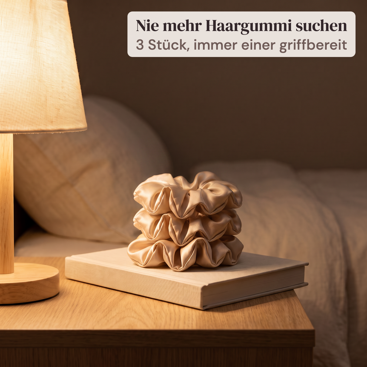 Drei Seloa Seiden-Scrunchies in Champagner gestapelt auf dem Nachttisch neben der Lampe